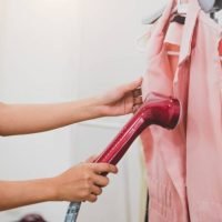 steam-iron Woman using steaming iron to ironing fashion shirt in laundry room. Girl doing stream vapor iron for press clothes in hand. Launder concentrate work and delivery to customer. Part time job occupation